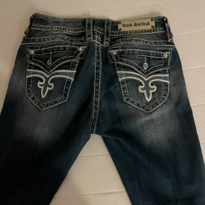 Mörkblå jeans från Rock Revival - Snygga mörkblå jeans från Rock Revival med unika broderade detaljer på bakfickorna. Säljer då de är förstora för mig. Strl W29 L34