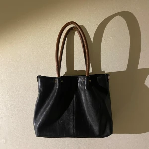 Svart handväska med bruna handtag - Snygg svart handväska med bruna handtag i skinn