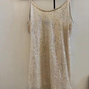 Glittrig klänning i champagne - Säljer en superglittrig klänning i champagnefärg med paljetter över hela. Den är ärmlös och perfekt för en festlig kväll. Klänningen har en kort längd och en normal passform.  ✨