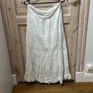 Vit långkjol med spetsdetaljer - Charmig vit långkjol med vackra spetsdetaljer. Kjolen har en luftig och romantisk stil, perfekt för varma dagar. Den är designad med flera lager av spets och tyg som ger en fin volym. Köpt utomlands för ca 400kr o är för kort på mig som är 175 💕
