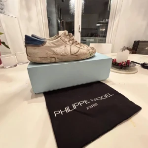 Sneakers från Philippe Model - Snygga sneakers från Philippe Model i beige med blå detaljer. Skorna har en klassisk snörning och en stilren design. Perfekta för en avslappnad look.