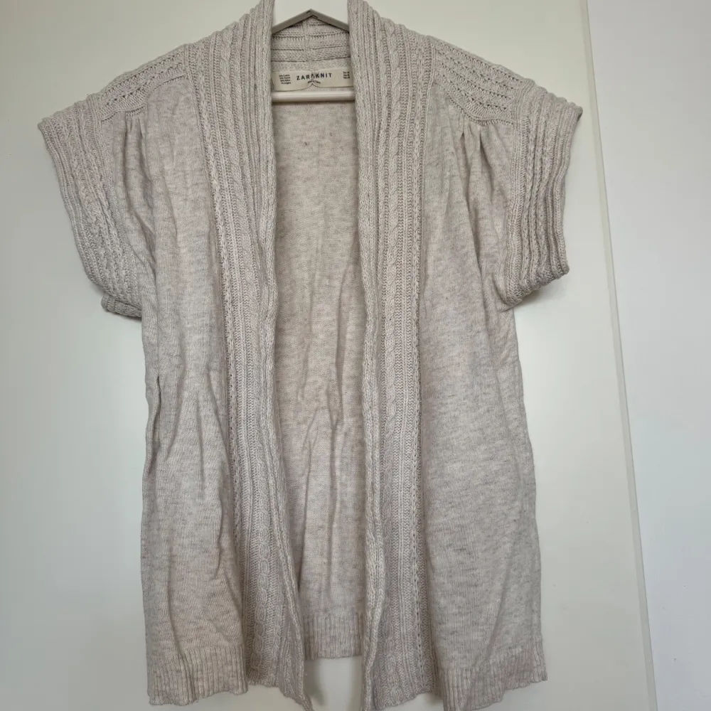 Säljer en supermysig beige stickad kofta från Zara Knit. Den är gjord av en blandning av bomull, viskos, nylon och angora, vilket gör den både mjuk och varm. Koftan har korta ärmar och en öppen design, perfekt för lager-på-lager under hösten. Den är använd men i bra skick och redo för en ny ägare!. Tröjor & Koftor.