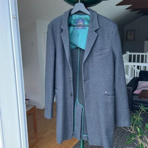 Grå kappa från Dstrezzed - Säljer en stilren grå kappa från Dstrezzed. Helt oanvänd! Den har en klassisk design med knappar framtill och en elegant krage. Fodret är i en snygg grön färg med små prickar, vilket ger en fin kontrast. Perfekt för höst och vår. (Nypris 2000 kronor)