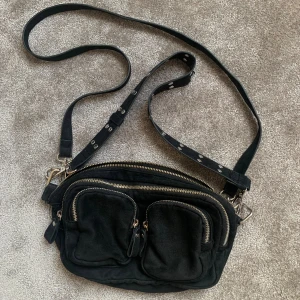 Svart väska  - Säljer denna populära väskan från Gina Tricot 🖤 Väskan har totalt 5 fack men tyvärr har dragkedjan gått sönder på det största facket (se sista bilden) 2 band ingår. Väskan är 30 cm bred och 15 cm hög 😊kom priv för mer info 