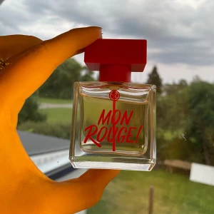 Mon Rouge Parfym - Säljer en elegant och stilren parfymflaska från Yves Rocher. Flaskan är fyrkantig och genomskinlig med en röd kork och texten 'Mon Rouge!' i rött på framsidan. Perfekt för den som älskar en fräsch och modern doft. Värde 499, Mitt pris 280, Nästitill oanvänd