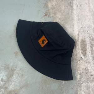 Carhartt Bucket Hat är en snygg vardagskompis för soliga dagar. Den robusta bomullskonstruktionen garanterar hållbarhet och komfort.  Material:  100% bomull Mått: 20 cm diameter 