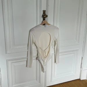 Vit långärmad bodysuit från Gina Tricot - Säljer en stilren vit långärmad bodysuit från Gina Tricot. Den har en öppen rygg med knytning. Perfekt för både vardag och fest! Använd 1 gång