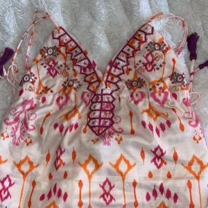 Mönstrad topp med broderi - Säljer en superfin topp med färgglatt mönster med smala axelband,  v-ringad och snyggt broderad på framsp. Perfekt för sommaren och festliga tillfällen! ❕har sytt in banden 3 cm då dem var för långa. banden är 31 cm långa nu och har endast använt den en gång 💗köptes för 300kr