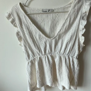Vit topp från Pull & Bear - Säljer en superfin vit topp från Pull & Bear. Den har en v-ringad design med volangdetaljer på ärmarna och en lätt ribbad struktur. Perfekt för sommardagar eller en avslappnad fest. Toppen är i nyskick och gjord av ett bekvämt material.