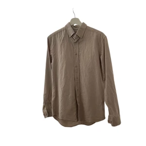 Brun långärmad skjorta - Säljer en stilren brun långärmad skjorta. Perfekt för höst och vinter med sin klassiska design och bekväma passform. Skjortan har knappar hela vägen ner och en traditionell krage. Passar både till vardags och lite finare tillfällen.