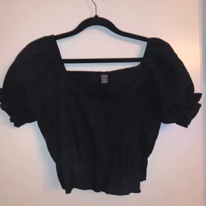 Svart topp från Shein - Säljer en snygg svart topp från Shein i storlek M. Toppen har en v-ringad design och korta puffärmar som ger en söt look. 