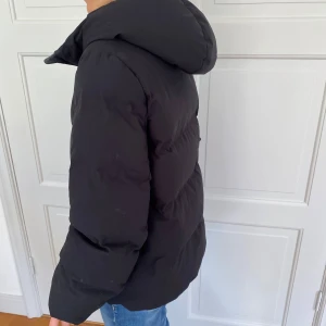 Svart pufferjacka med huva - Säljer en svart pufferjacka som är perfekt för kalla dagar. Jackan har en skön huva och stängs med dragkedja. Den är långärmad och har en normal passform, vilket gör den superbekväm att bära. Perfekt för både höst och vinter!Storlek s men passar xs-m