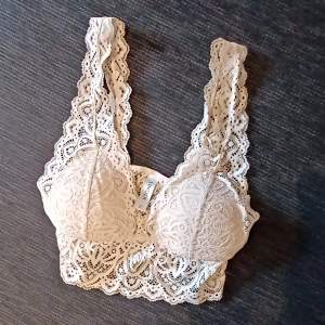 Säljer en superfin beige spets bralette från Lindex. Den har ett vackert spetsmönster och breda axelband som ger extra stöd. Perfekt för att ha under en blus eller bara som den är för en chic look. Använd ett fåtal gånger, så den är i bra skick!