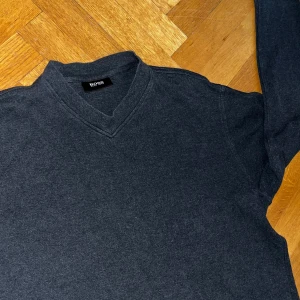 Mörkgrå tröja från Hugo Boss - Säljer en stilren mörkgrå tröja från Hugo Boss. Den har en klassisk v-ringning och är perfekt för både vardag och lite finare tillfällen. Tröjan är i bra skick och passar perfekt till höst- och vintergarderoben. Skön och enkel att matcha med det mesta!