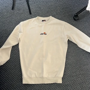 Beige sweatshirt från Ellesse - Säljer en snygg beige sweatshirt från Ellesse i storlek S. Tröjan har en klassisk design med ribbade muddar och en liten broderad logga på bröstet. Perfekt för en avslappnad stil och passar till alla årstider. Skön och stilren, ett måste i garderoben!