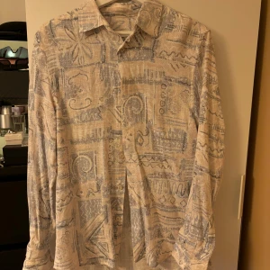 Mönstrad skjorta i blått och beige - Säljer en unik och stilren långärmad skjorta med ett abstrakt mönster i blått och beige. Skjortan har knappar framtill och en klassisk krage. Perfekt för både vardag och festliga tillfällen!