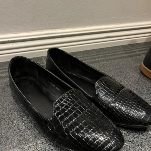 Svarta loafers med krokodilmönster - Snygga svarta loafers i skinn med ett coolt krokodilmönster. Perfekta för både vardag och fest! De har en klassisk design med en bekväm passform. Ett måste för garderoben om du vill ha något stilrent och tidlöst.