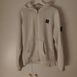 Säljer en snygg vit zip hoodie från Stone Island. Den är i bra skick och superbekväm att ha på sig. Passar perfekt till höst och vår! Sitter perfekt som M. Priset är inte hugget i sten!