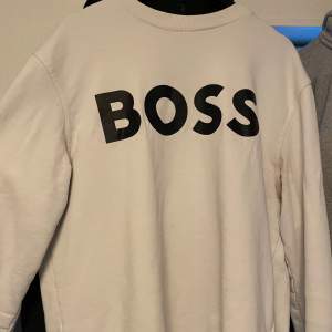 Säljer en stilren vit sweatshirt från BOSS i mycket bra skick. Den har en stor BOSS-logga på framsidan och är perfekt för både vardag och avslappnade tillfällen. Tröjan är långärmad och gjord i ett mjukt material som känns skönt mot huden. Passar perfekt till jeans eller joggers!