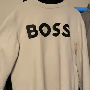 Säljer en stilren vit sweatshirt från BOSS i mycket bra skick. Den har en stor BOSS-logga på framsidan och är perfekt för både vardag och avslappnade tillfällen. Tröjan är långärmad och gjord i ett mjukt material som känns skönt mot huden. Passar perfekt till jeans eller joggers!