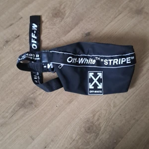 Svart magväska från Off-White - Säljer en cool svart magväska från Off-White med texten 'STRIPE' och deras ikoniska logga. Väskan har en justerbar rem med Off-White-tryck och en dragkedja för säker förvaring. Perfekt för att bära det nödvändigaste med stil!