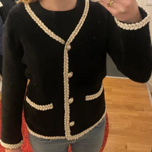 Svart kofta med vita detaljer - Säljer en superfin svart kofta med vita flätade detaljer längs kanterna och knappar framtill. Den har två fickor och är perfekt för både vardag och fest. Koftan är i bra skick och passar perfekt till höst och vinter. ❣️❣️