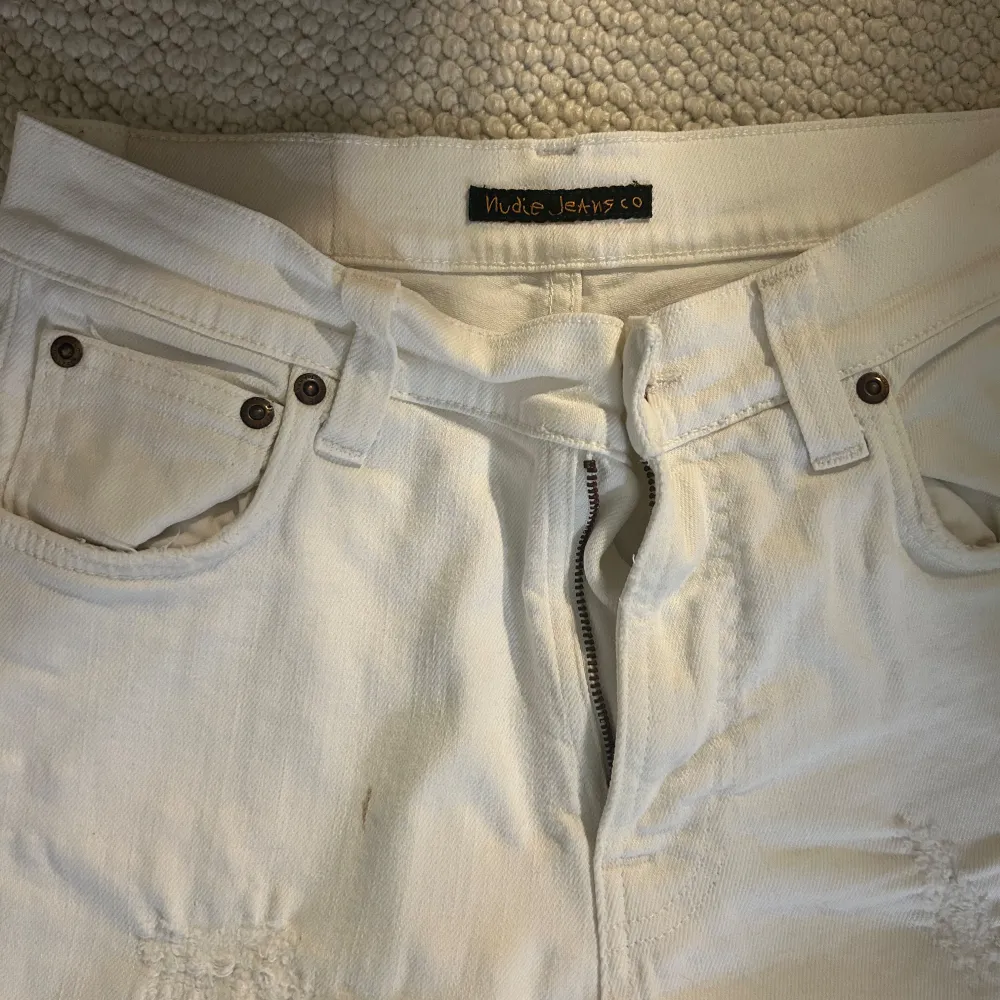 Säljer ett par vita jeans från Nudie Jeans i storlek 26/30. De har en snygg distressed look med slitningar på framsidan. De är i bra skick, förutom en litenliten fläck till vänster(på bild) om dragkedjan. . Jeans & Byxor.