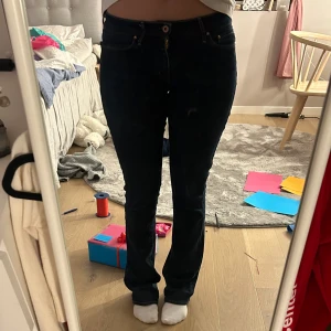 Mörkblå bootcut jeans - Säljer ett par mörkblå bootcut jeans i mycket bra skick. De har en midwaist passform och är perfekta för både vardag och fest. Jeansen har klassiska fem fickor och en knappgylf. Superbekväma och stilrena! Lite slitna ner till