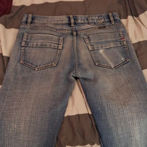 Blå jeans från Diesel - Säljer ett par snygga blå jeans från Diesel i bra skick. De har en klassisk femficksdesign med coola detaljer som logotyp på bakfickan och en liten ficka fram. Perfekta för vardagsbruk eller en avslappnad utekväll. Passformen är normal och de är tillverkade i slitstarkt denim. 