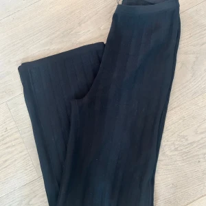 Svarta ribbade byxor från Totême - Säljer ett par svarta ribbade byxor från Totême i storlek XS. De är tillverkade av 85% rayon och 15% nylon, vilket gör dem både bekväma och stretchiga. Perfekta för en stilren och avslappnad look.