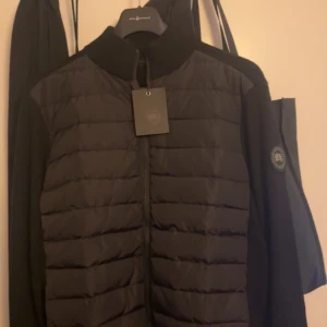 Svart pufferjacka från Canada Goose - Säljer en svart pufferjacka från Canada Goose i nytt skick. Jackan har en stilren design med dragkedja och långärmade ärmar. Perfekt för höst och vinter, håller dig varm och snygg. Storleken är herr M. Passar både till vardags och lite finare tillfällen. Pris går att diskutera. Kvitto finns. 