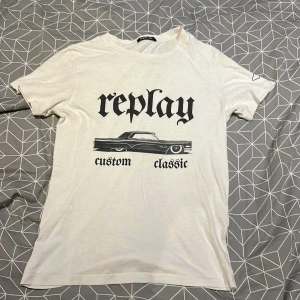 Vit t-shirt från Replay - Säljer en vit t-shirt från Replay med coolt tryck av en klassisk bil och texten 'custom classic'. Perfekt för en avslappnad stil. Skön och lätt att bära!
