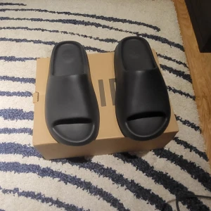 Yeezy Slides Onyx - Säljer ett par svarta Yeezy Slide från Adidas i storlek herr 43. De är i nytt skick och kommer i originalförpackning. Perfekta för en avslappnad stil och bekväma att bära hela dagen.