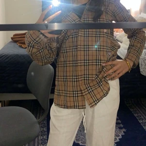 Rutig skjorta från Burberry - Säljer en klassisk rutig skjorta från Burberry i beige, svart och röd. Skjortan har långa ärmar och knappar framtill. Endast använd 1 gång, storlek XL men skulle säga att den sitter som S (jag har XS/S). Priset går att diskuteras vid snabb affär. 