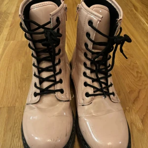 Rosa boots med snörning och dragkedja - Säljer ett par snygga rosa boots i syntetmaterial. De har både snörning och dragkedja för enkel på- och avtagning. Perfekta för höst och vår med sin coola stil och bekväma passform. De har en glansig finish som ger en extra touch till din outfit. De är lite trasiga men det går säkert att laga om man är händig eller lämna in de till en skomakare. 