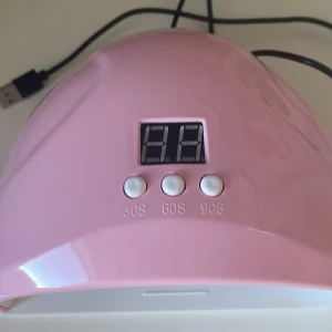 Rosa UV-lampa för naglar med timer - Säljer en rosa UV-lampa för naglar med digital display och tre tidsinställningar: 30, 60 och 90 sekunder. Perfekt för att härda gelnagellack snabbt och enkelt hemma. Den har en USB-anslutning för smidig användning. Lampan är kompakt och lätt, vilket gör den enkel att förvara och ta med sig.