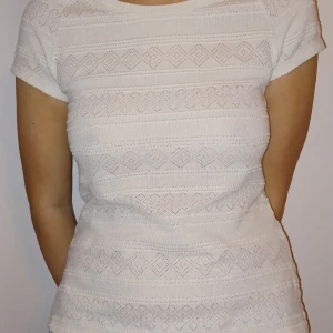 Vit stickad topp - Säljer en söt vit stickad topp med korta ärmar. Den har ett diskret mönster som ger en fin textur och är perfekt för både vardag och fest. Toppen är i bra skick och passar till många olika outfits. Perfekt för vår och sommar!