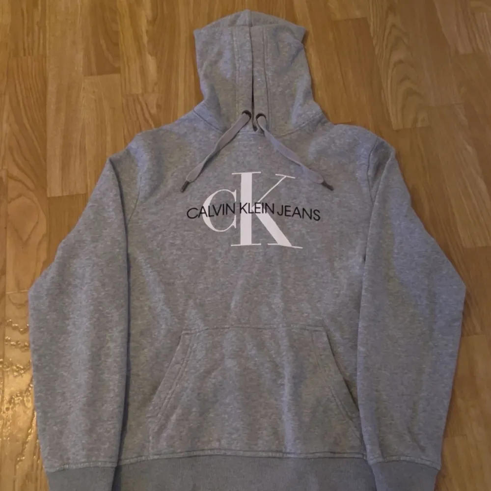 Säljer en snygg grå hoodie från Calvin Klein Jeans i storlek M. Den har en klassisk design med stor logga på framsidan och en bekväm huva med dragsko. Perfekt för en avslappnad stil och passar till alla tillfällen. Skön och stilren!. Tröjor & Koftor.