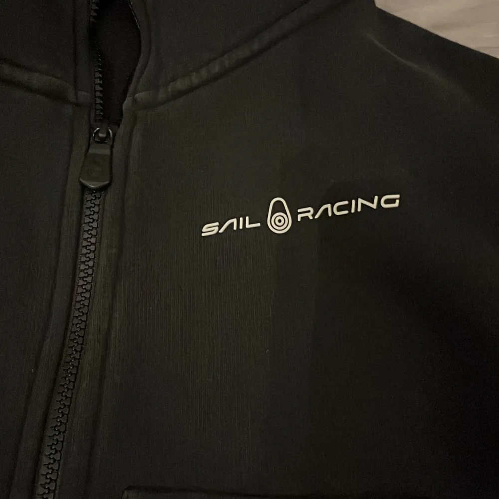 Säljer en svart hoodie från Sail Racing i mycket bra skick. Den har en dragkedja framtill och en praktisk huva. Perfekt för höst och vår, och den är superbekväm att ha på sig. Passar både till vardags och lite mer avslappnade tillfällen.. Jackor.