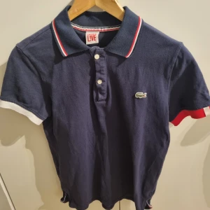 Lacoste pikétröja - Mörkblå pikétröja från Lacoste. Inga hål eller fläckar. Storlek 5 vilket motsvarar herrstorlek L men passar nog mer som M.