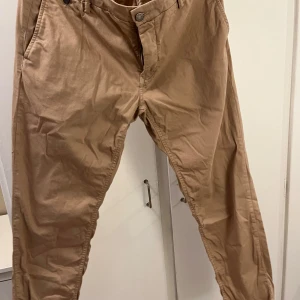 Beige byxor från Replay - Säljer ett par snygga beige byxor från Replay i bra skick. De har en normal passform och är perfekta för både vardag och fest. Byxorna har knappar och dragkedja framtill. Perfekta för höst och vår!
