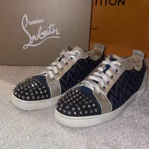 Säljer ett par feta Christian Louboutin sneakers i mycket bra skick! De har ett blått och silver zigzag-mönster med snygga nitar på toecapen Skorna har den klassiska röda sulan och är perfekta för att sticka till festen. Storlek 43-44