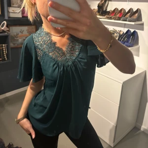 Grön blus med spetsdetaljer - Säljer en elegant grön blus med vackra spetsdetaljer vid halsringningen. .