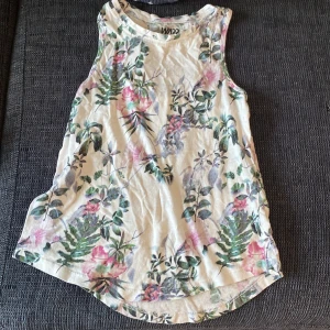 Blommig ärmlös topp från WNDZ - Säljer en superfin ärmlös topp från WNDZ med blommigt mönster i grönt och rosa. Toppen har en öppen ryggdetalj och är perfekt för sommardagar. Materialet är mjukt och bekvämt, vilket gör den idealisk för både vardag och fest. Passar perfekt till jeans shorts och kjolar