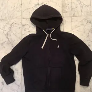 Säljer en svart hoodie från Ralph Lauren med dragkedja och klassisk logga på bröstet. Perfekt för höst och vinter. Litet slitage på ryggen som sytts ihop på nytt men annars i bra skick.