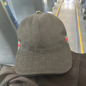 Gucci keps - Snygg svart keps. Kepsen har gröna och röda detaljer på sidorna. Perfekt för att ge din outfit en lyxig touch. Passar både till vardags och fest! Nytt skick inga tecken på användning storlek S