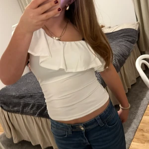 Vit offshoulder topp med volang - Säljer en superfin vit offshoulder topp med volangdetaljer. Perfekt för sommardagar eller en festlig kväll. Toppen är tight och framhäver figuren snyggt. Passar bra till både jeans och kjol. Använd ett fåtal gånger, så i mycket bra skick!