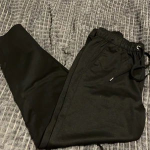 Svarta mjukisbyxor - Säljer ett par svarta mjukisbyxor i bra skick. De har en bekväm elastisk midja med snörning för justerbar passform. Perfekta för en avslappnad dag hemma eller en snabb tur till affären. Passar till alla säsonger och är ett måste i garderoben!