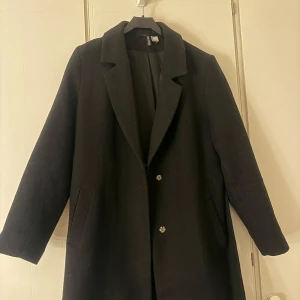 Svart kappa med knappar - Säljer en elegant svart kappa i storlek L. Den har en klassisk design med knappar framtill och en stilren krage. Perfekt för höst och vinter, och passar både till vardags och fest. Kappan är i mycket bra skick och redo för nya äventyr!
