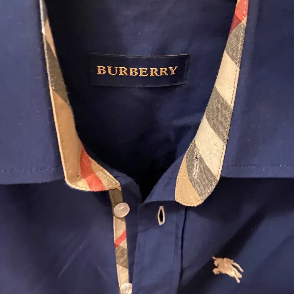 Snygg mörkblå skjorta från Burberry med Burberrys klassiska rutiga detaljer på insidan av kragen och ärmslutet. Köpt från Burberrys Egna affär i Paris. . Skjortor.